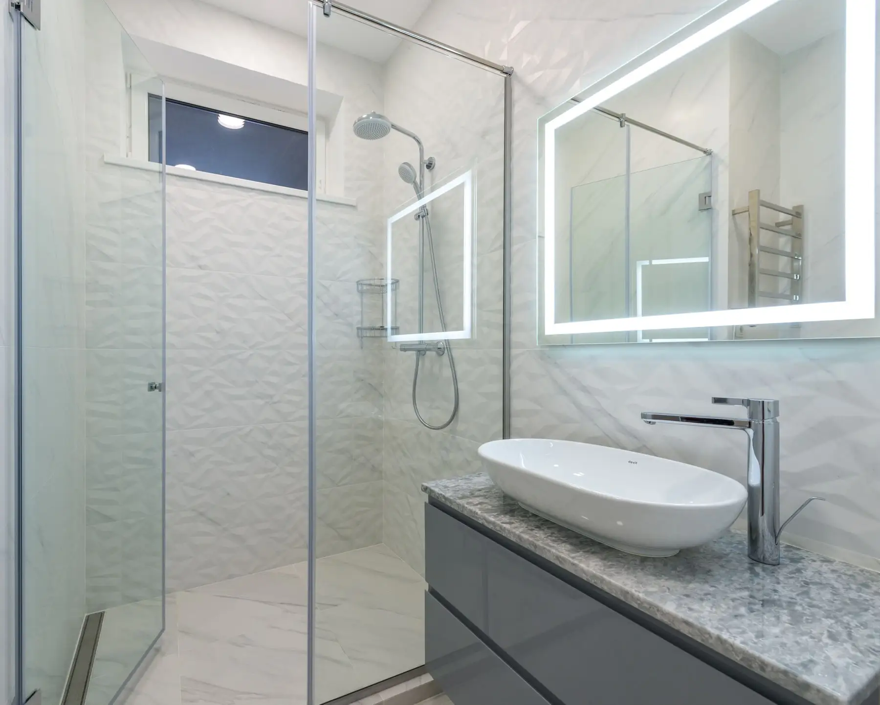 A new walk-in shower beside a stone-topped vanity