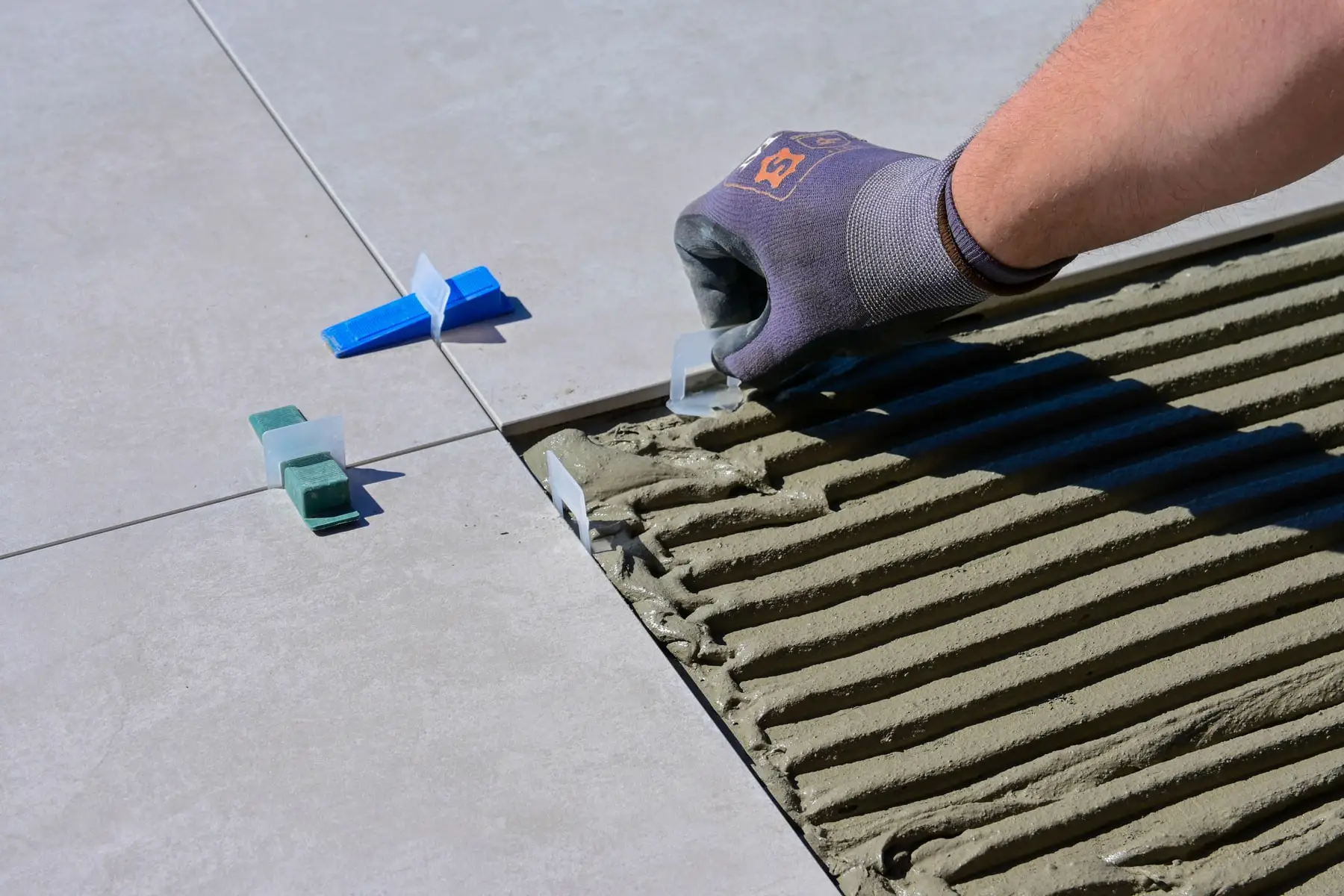 Large format floor tiles being laid on combed adhesive with levelling clips